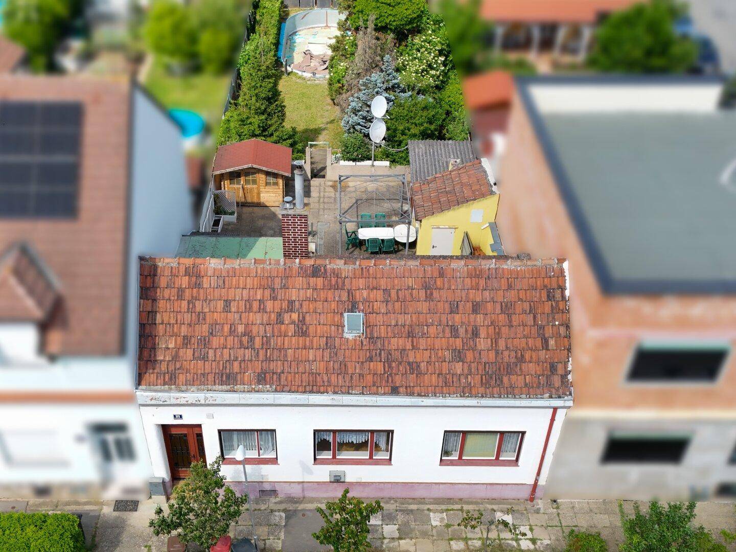 Luftaufnahme eines Hauses mit rotem Ziegeldach, Gartenhaus und gepflasterter Terrasse.