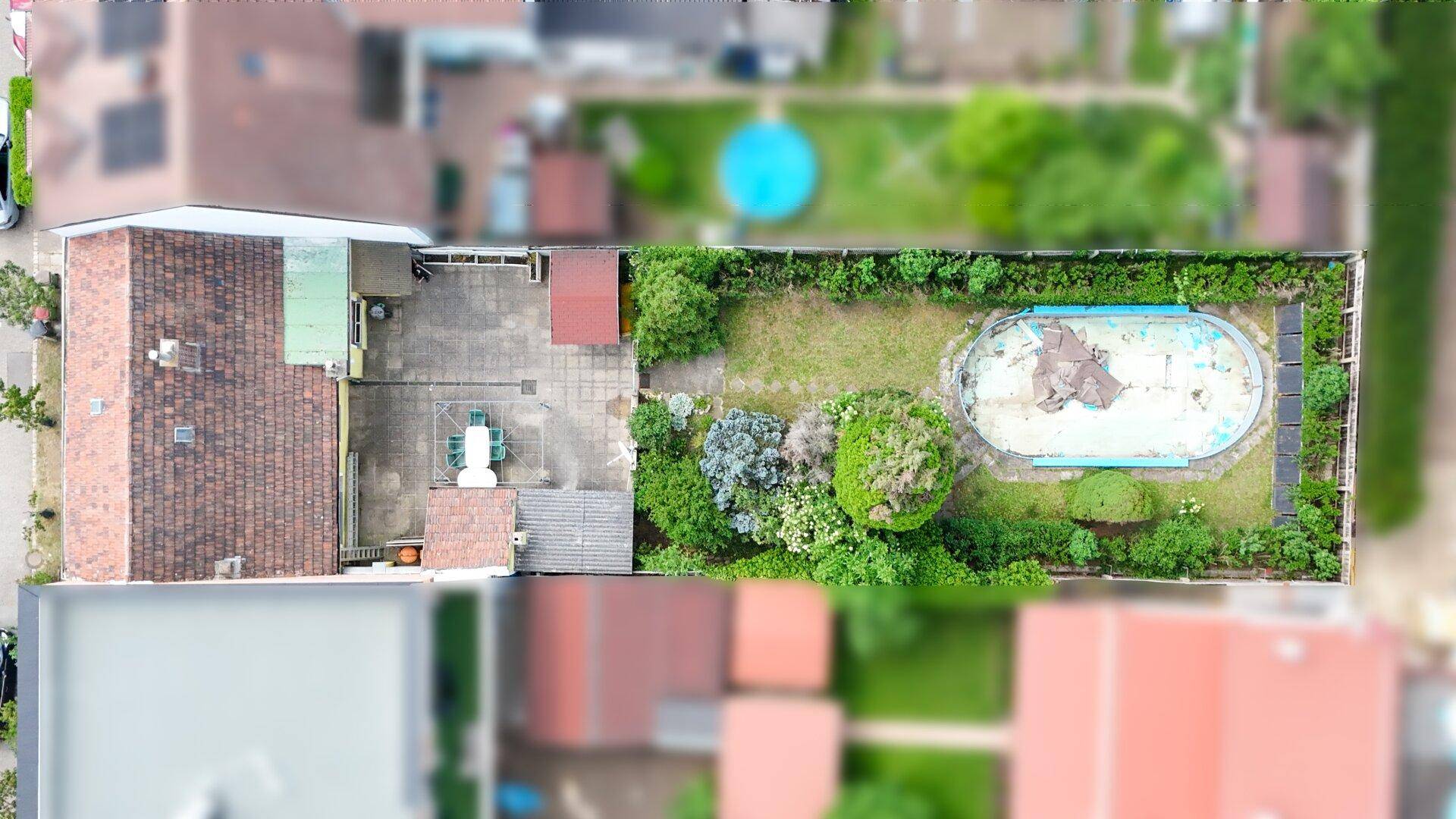 Vogelperspektive des Grundstücks mit Haus, großer Terrasse, Garten und leerem Pool.