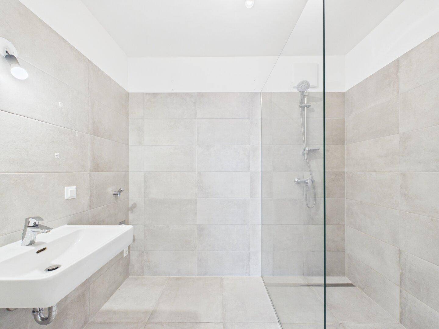 Modernes Badezimmer mit begehbarer Dusche, Waschbecken und hellgrauen Fliesen.
