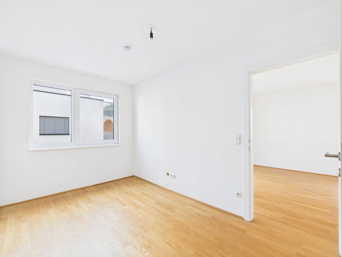 Helles, leeres Zimmer mit Holzboden und Fenster, bereit zur individuellen Gestaltung.