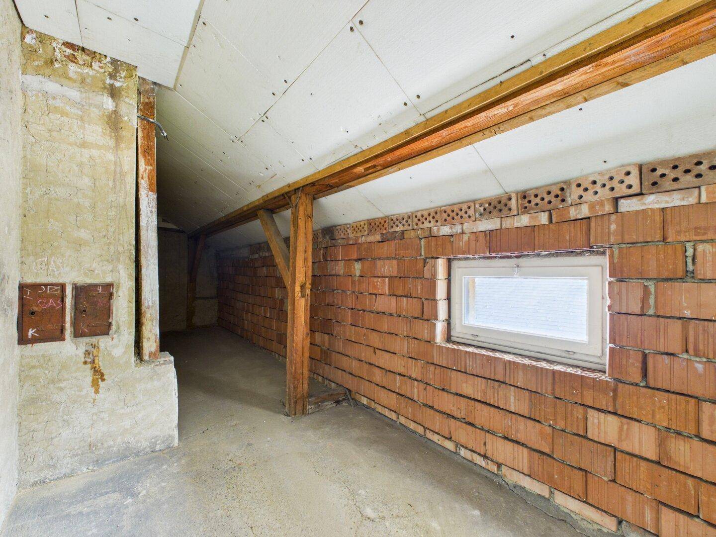 Unausgebauter Dachboden mit sichtbaren Ziegelwänden und Holzbalken, bietet Ausbaupotenzial.