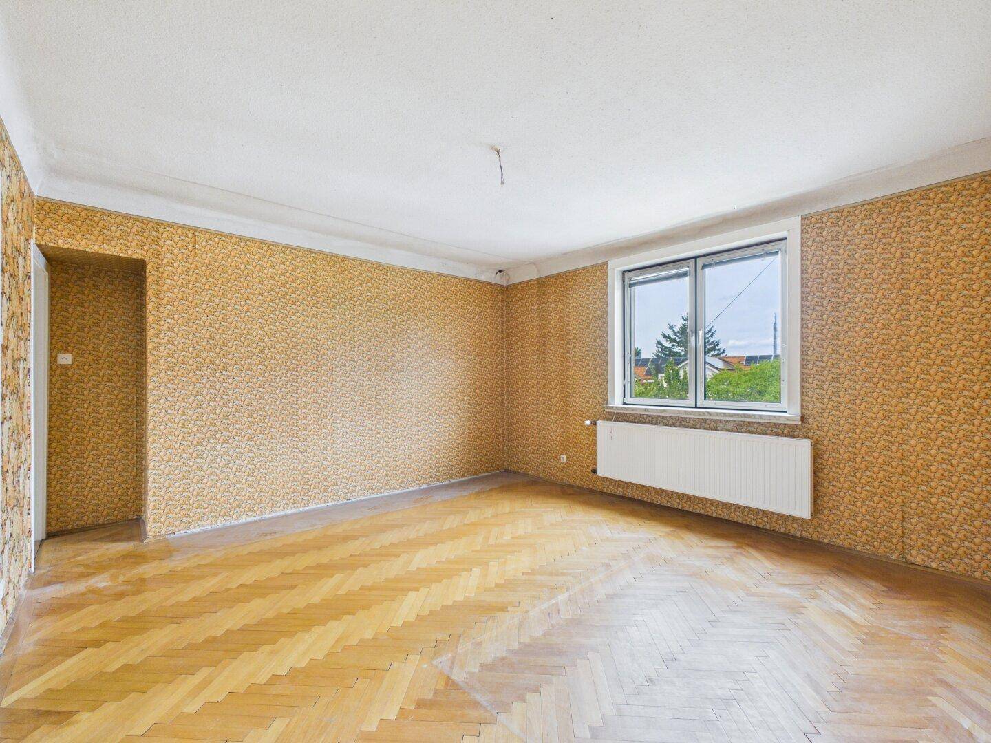 Gemütliches Zimmer mit Fischgrätparkett und gemusterter Tapete, bietet Potenzial für individuelle Gestaltung.