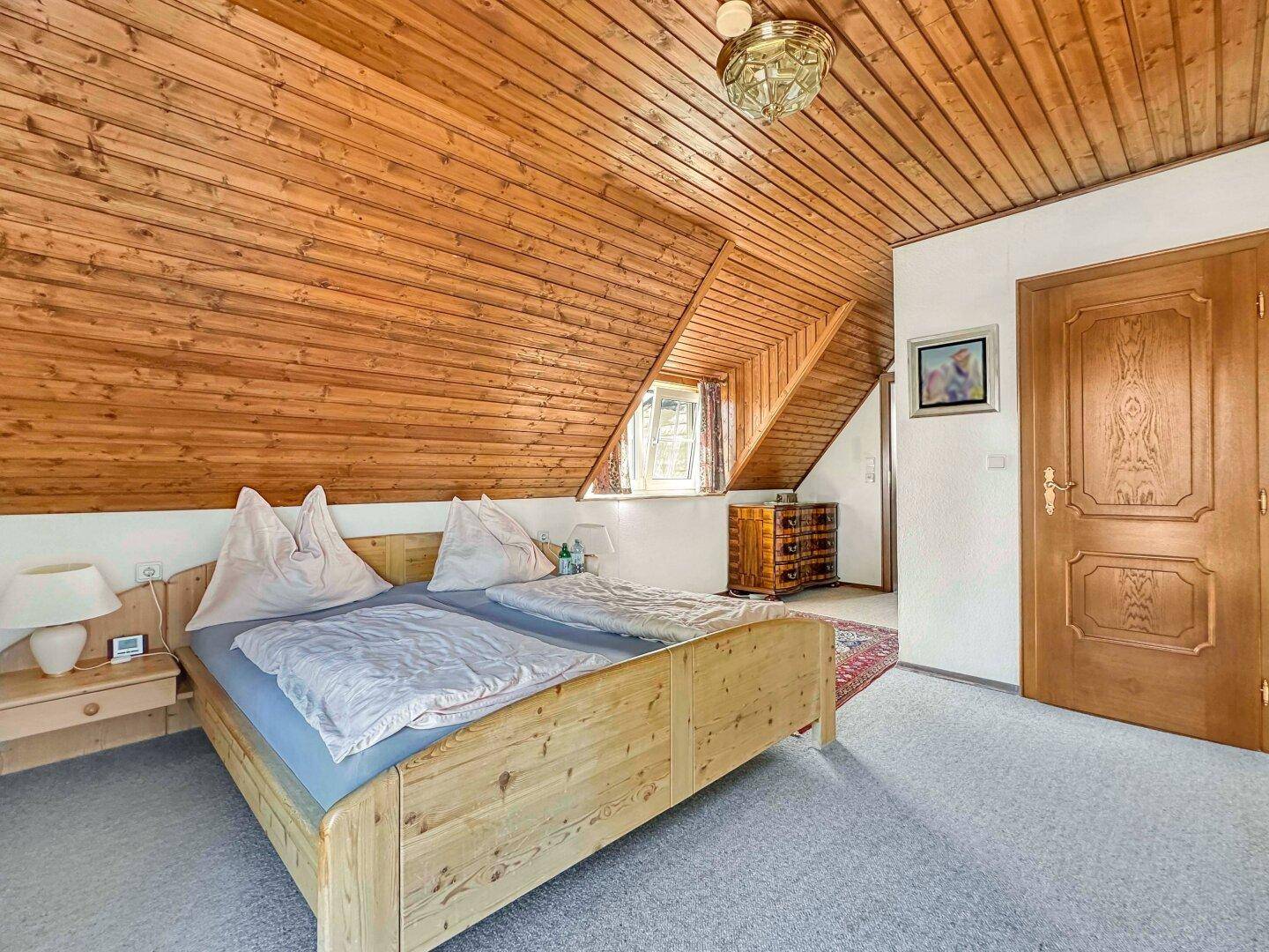 Gemütliches Schlafzimmer mit Holztäfelung an Decke und Dachschrägen, sowie Teppichboden.