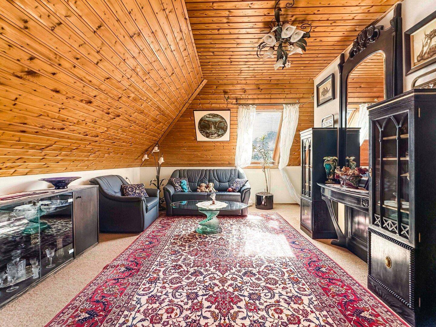 Geräumiges Wohnzimmer mit Holztäfelung, Dachschrägen und einem großen Orientteppich.