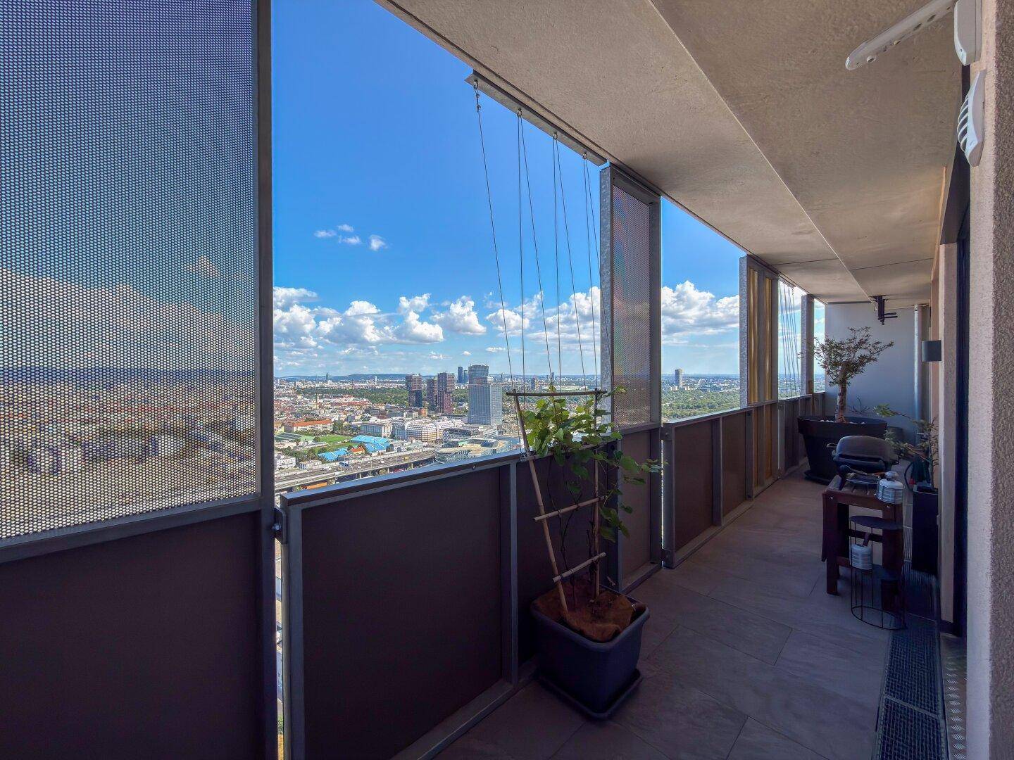 Langer Balkon mit perforierten Sichtschutzwänden, Pflanzen und Grill, bietet weiten Stadtblick.