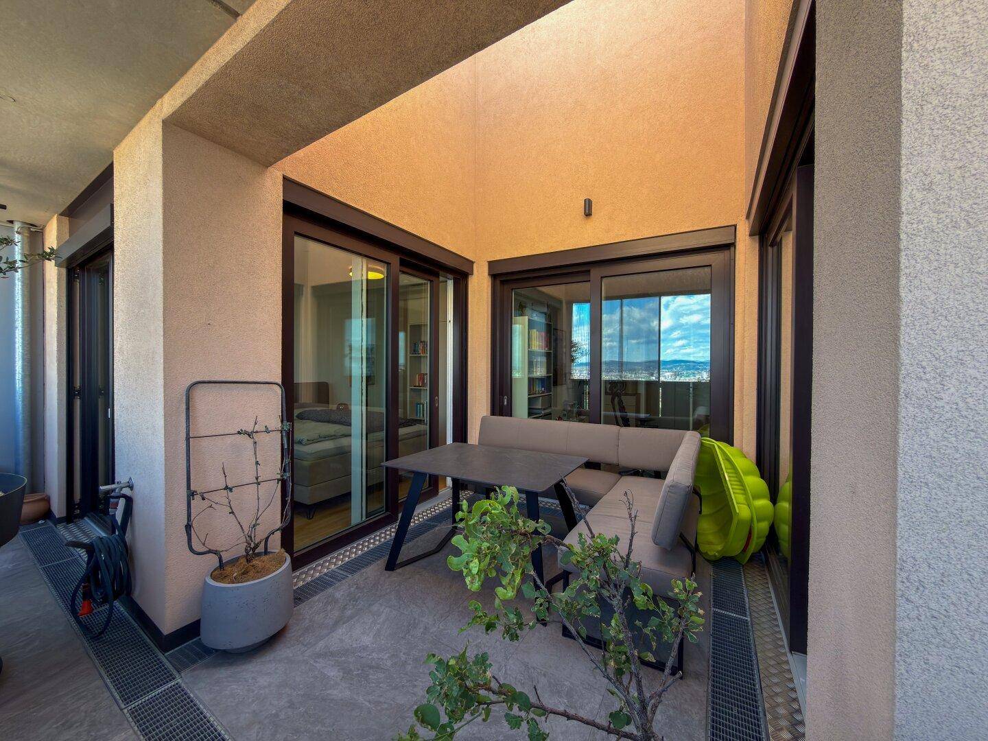 Gemütlicher Eckbalkon mit Outdoor-Sitzgruppe, Pflanzen und Zugang zu den Innenräumen.