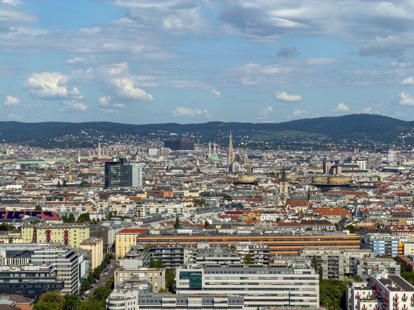 Dichter Stadtblick mit historischen Gebäuden, moderner Architektur und hügeliger Landschaft im Hintergrund.