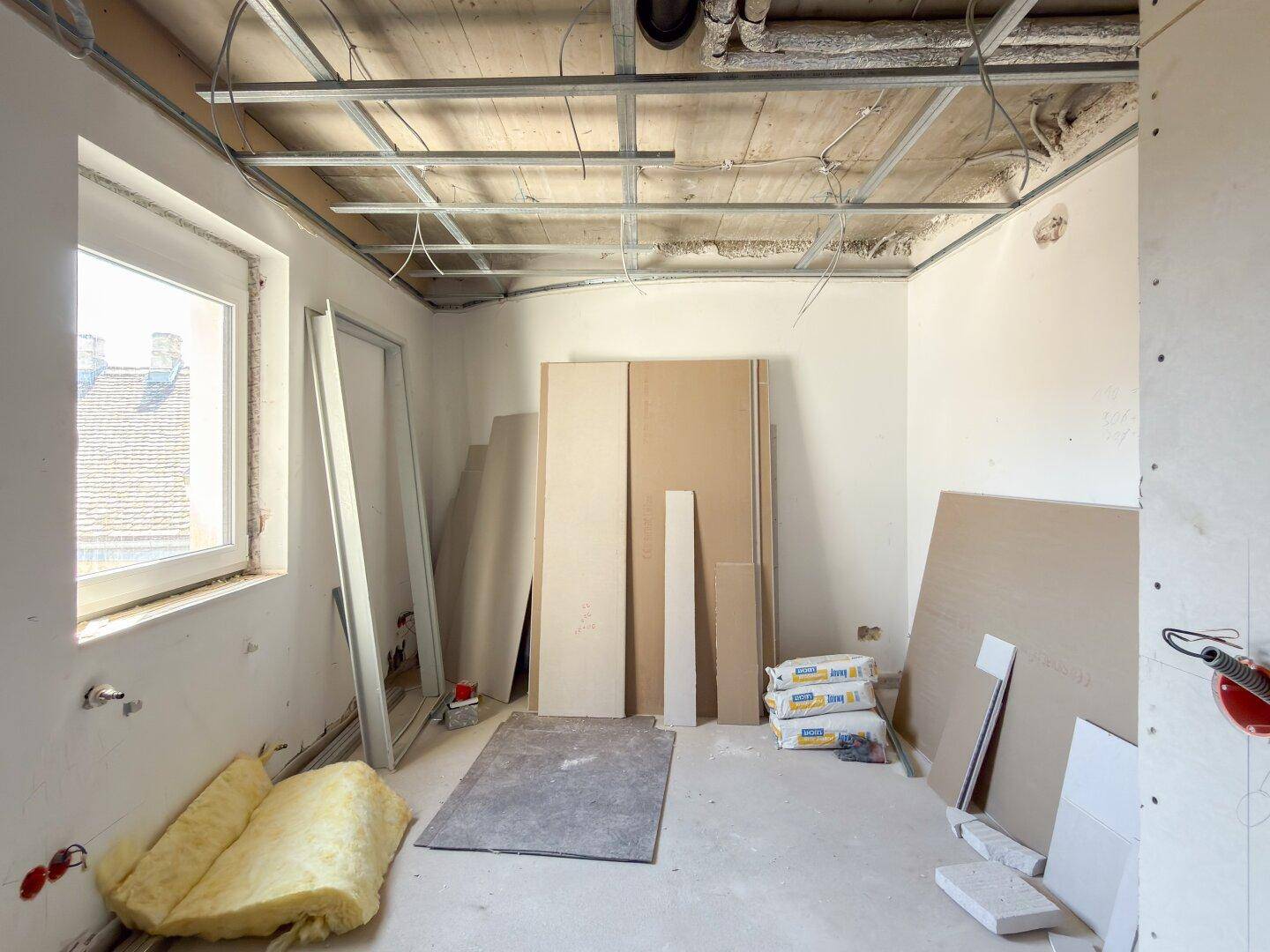Unfertiger Raum mit Fenster, Deckenkonstruktion und Baumaterialien.