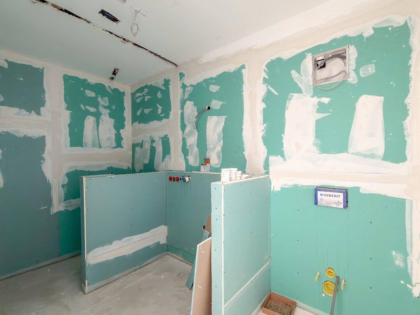 Badezimmer im Rohbau mit grünen Trockenbauwänden und sichtbaren Installationen.
