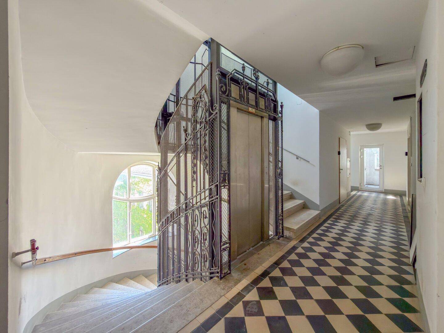 Historischer Eingangsbereich mit kunstvollem Aufzug und Schachbrettmuster-Boden.