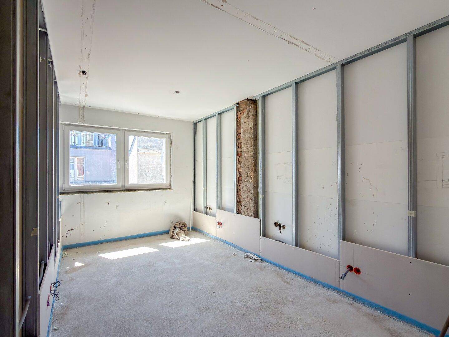 Innenraum im Rohbau mit Fenster und vorbereiteten Wänden für die weitere Gestaltung.