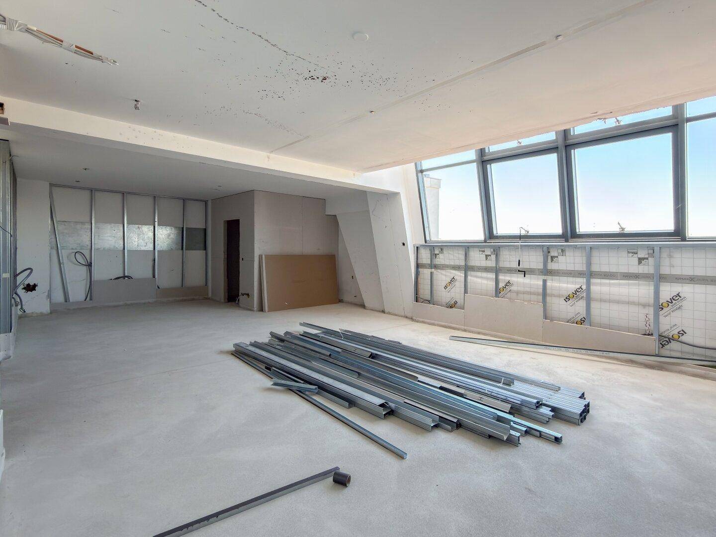 Heller Innenraum im Bauzustand mit Metallständerwerk und weitem Ausblick durch die Fenster.