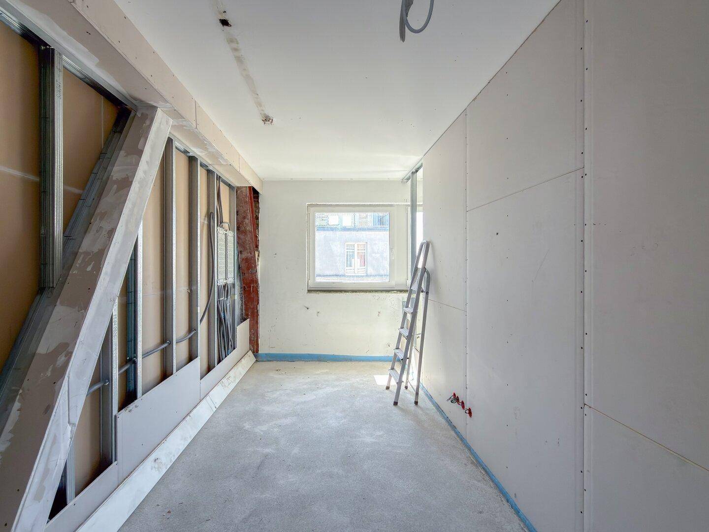 Baustelle eines Zimmers mit Trockenbauwänden und einem Fenster, das Tageslicht hereinlässt.