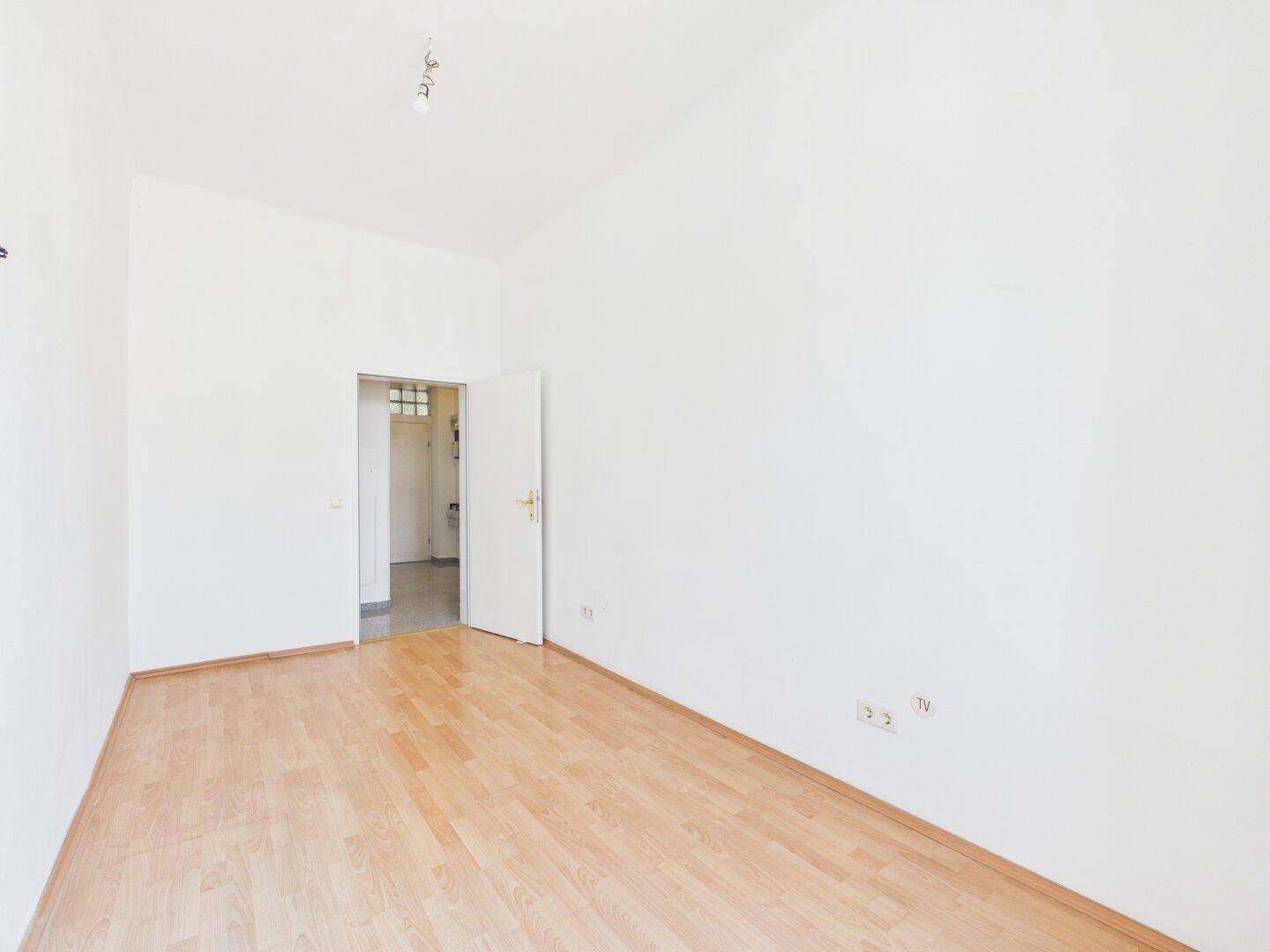 Leeres Zimmer mit Laminatboden und weiß gestrichenen Wänden, bietet vielseitige Nutzungsmöglichkeiten.
