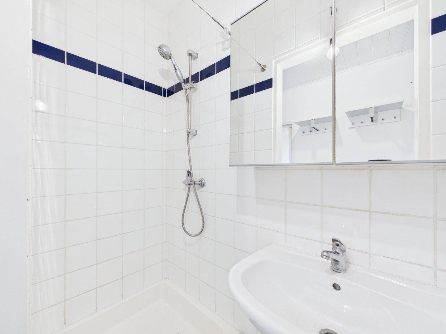 Modernes Badezimmer mit weißen Fliesen, Dusche und Spiegelschrank, funktional und hell.