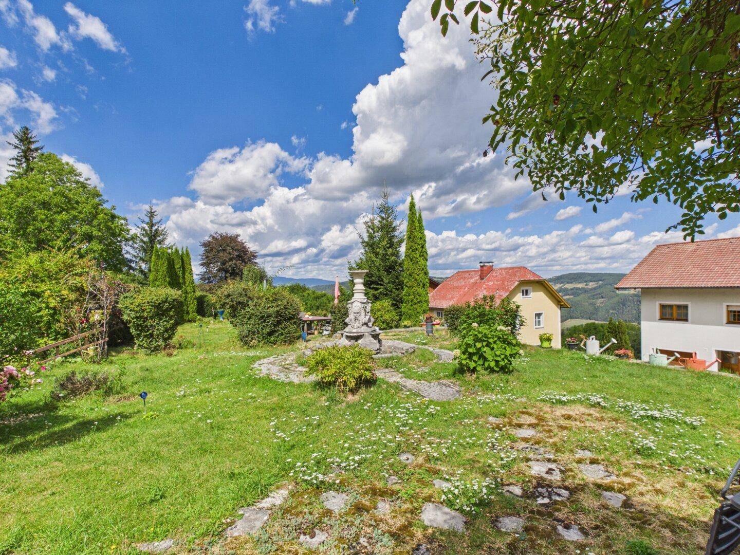 Weitläufiger Garten mit Rasenfläche, Zierbrunnen und Panoramablick auf die hügelige Landschaft.