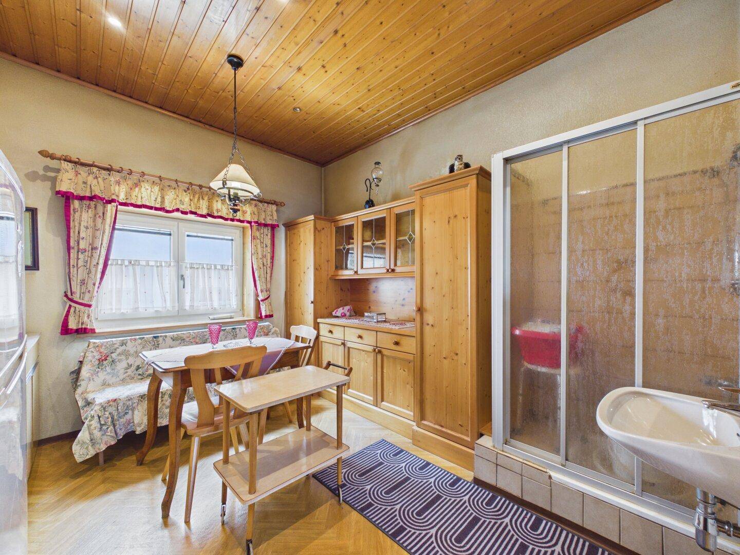 Rustikale Wohnküche mit Holzmöbeln, Holzboden und einer Duschkabine im Raum.