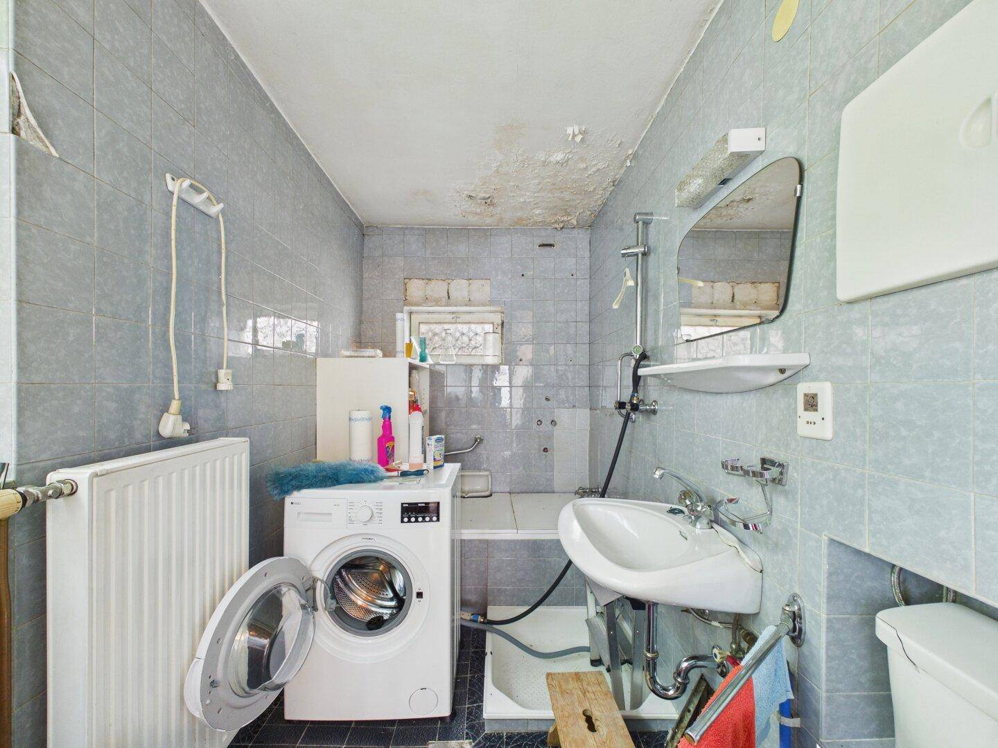 Älteres Badezimmer mit hellblauen Fliesen, Waschmaschine und einfacher Ausstattung.