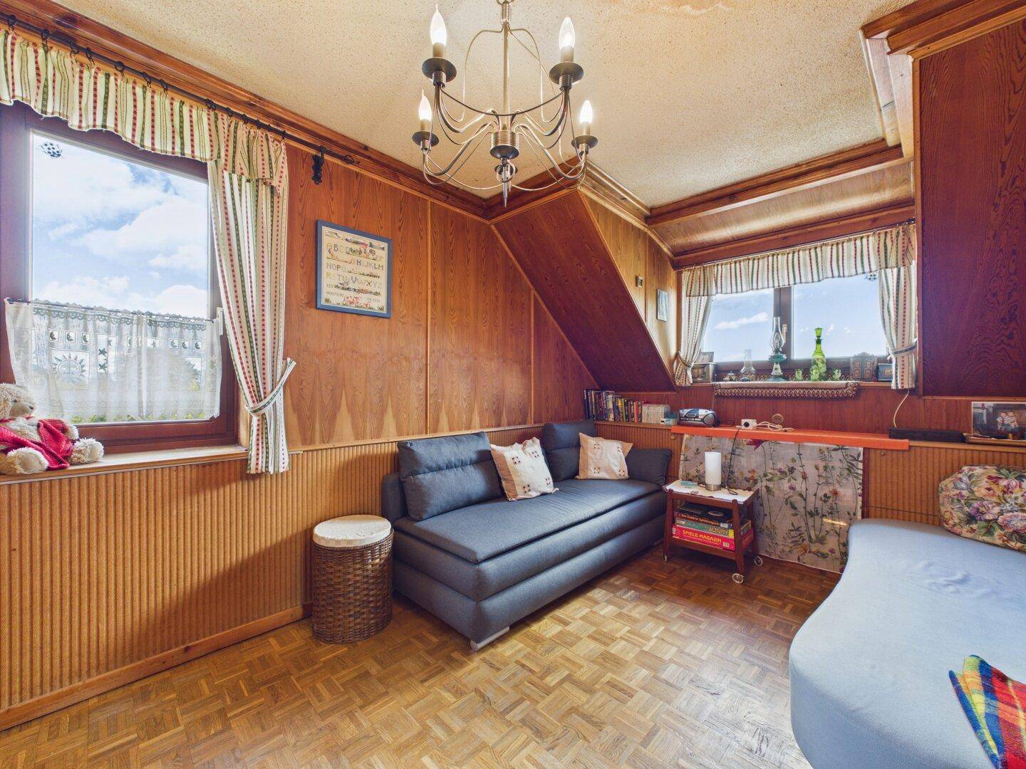 Gemütliches Wohnzimmer mit Holzvertäfelung, Holzboden und Dachschrägen.