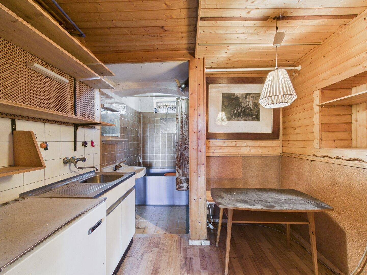 Kleine Küche mit Holzvertäfelung, einfacher Ausstattung und Zugang zu einem Badezimmer.