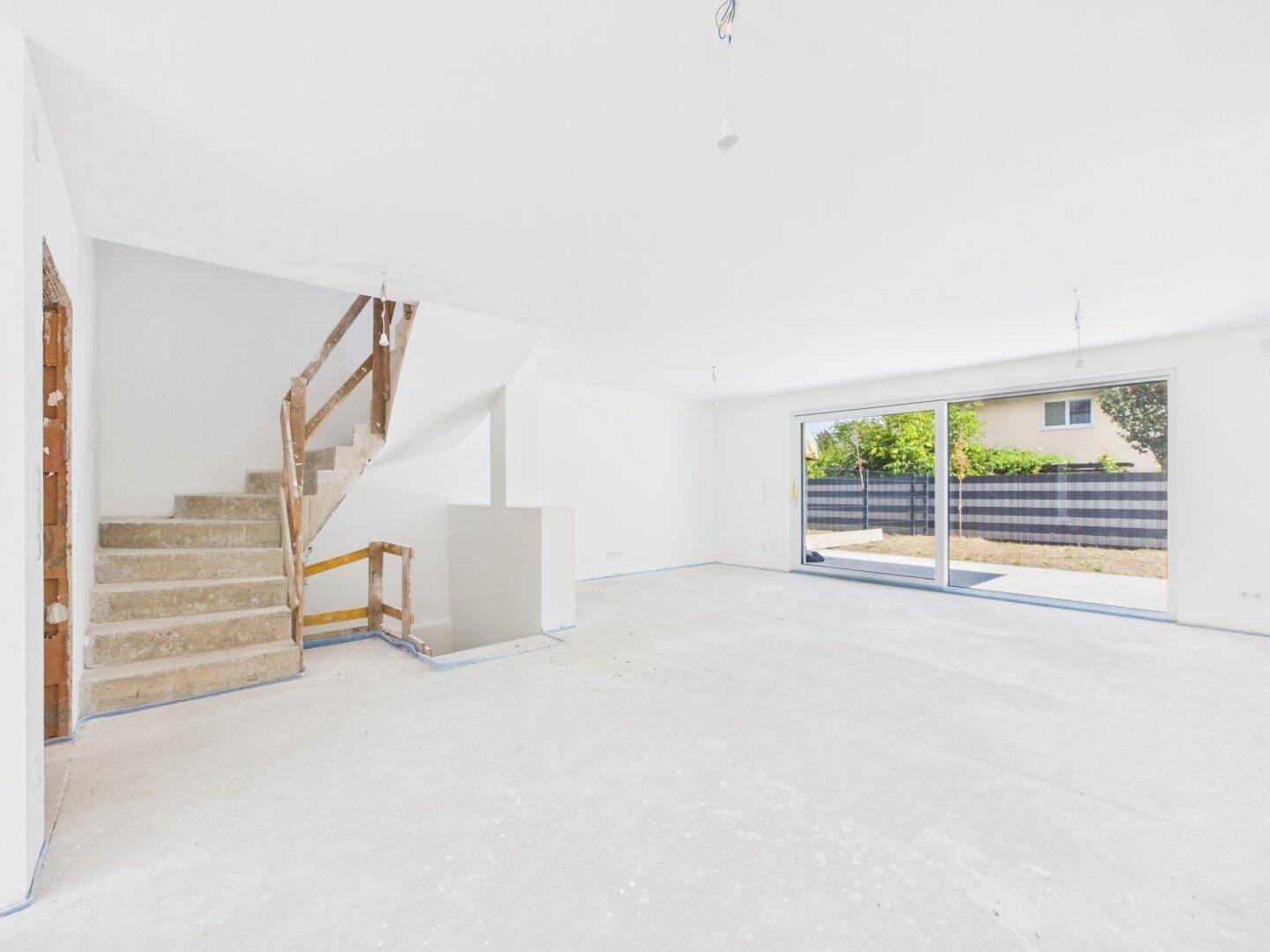 Heller, unmöblierter Wohnbereich im Rohbau mit Zugang zum Garten.
