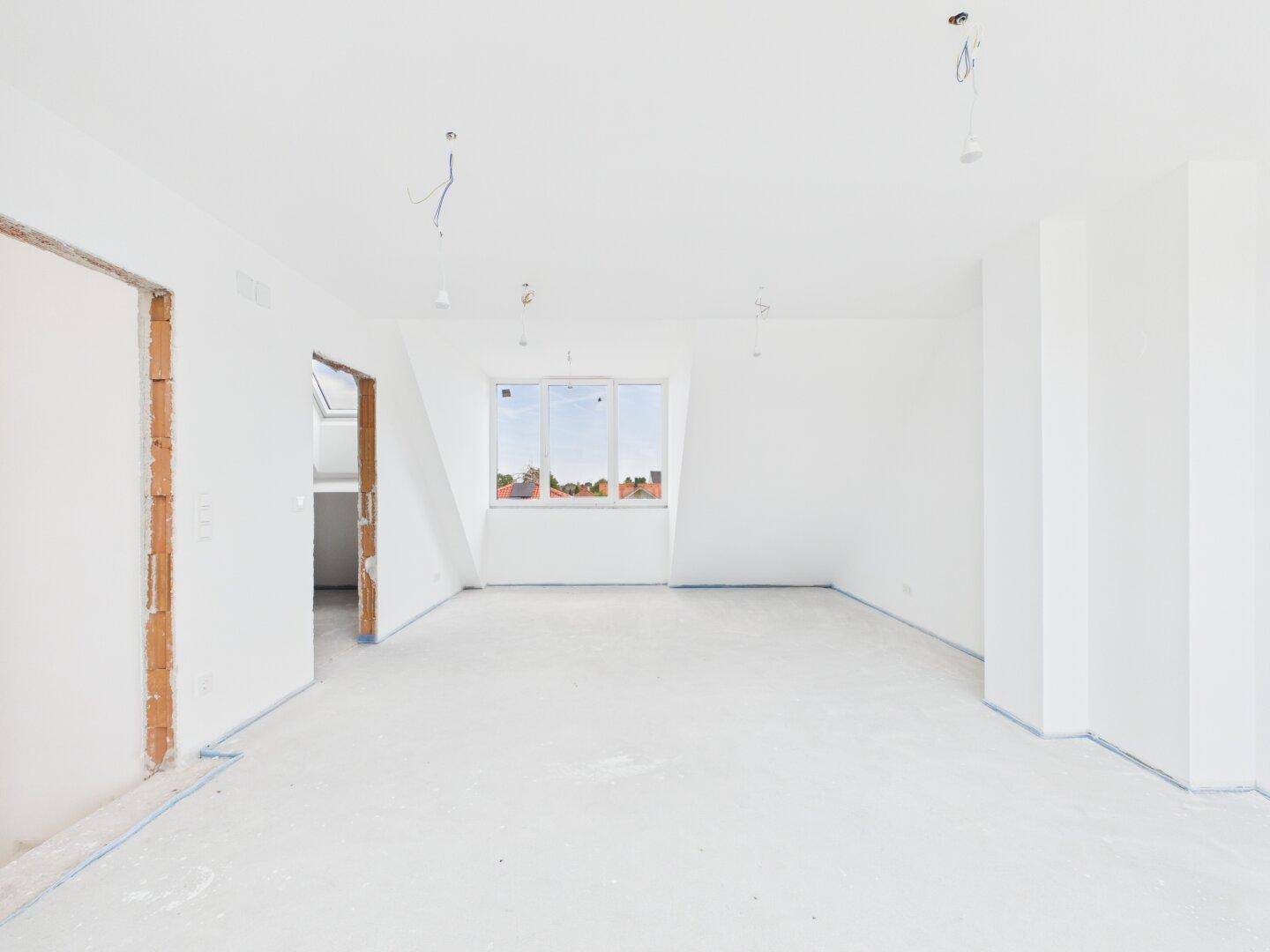 Großer, unmöblierter Dachgeschossraum im Rohbau mit Dachgaubenfenster.