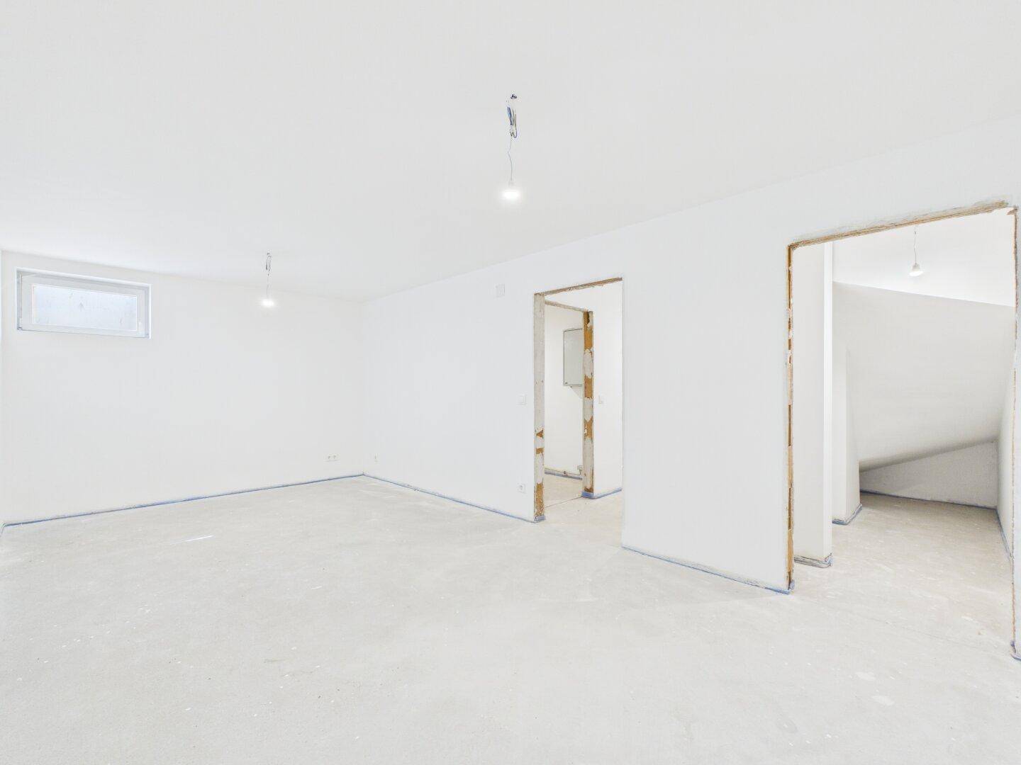 Geräumiger, unmöblierter Dachgeschossraum im Rohbau mit Fenster.