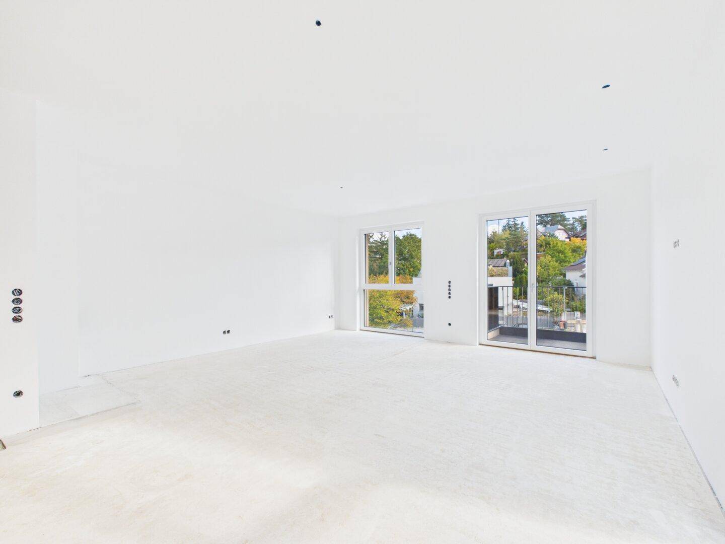 Geräumiger, heller Wohnbereich im Rohbau mit großen Fenstern und Zugang zu einem Balkon.