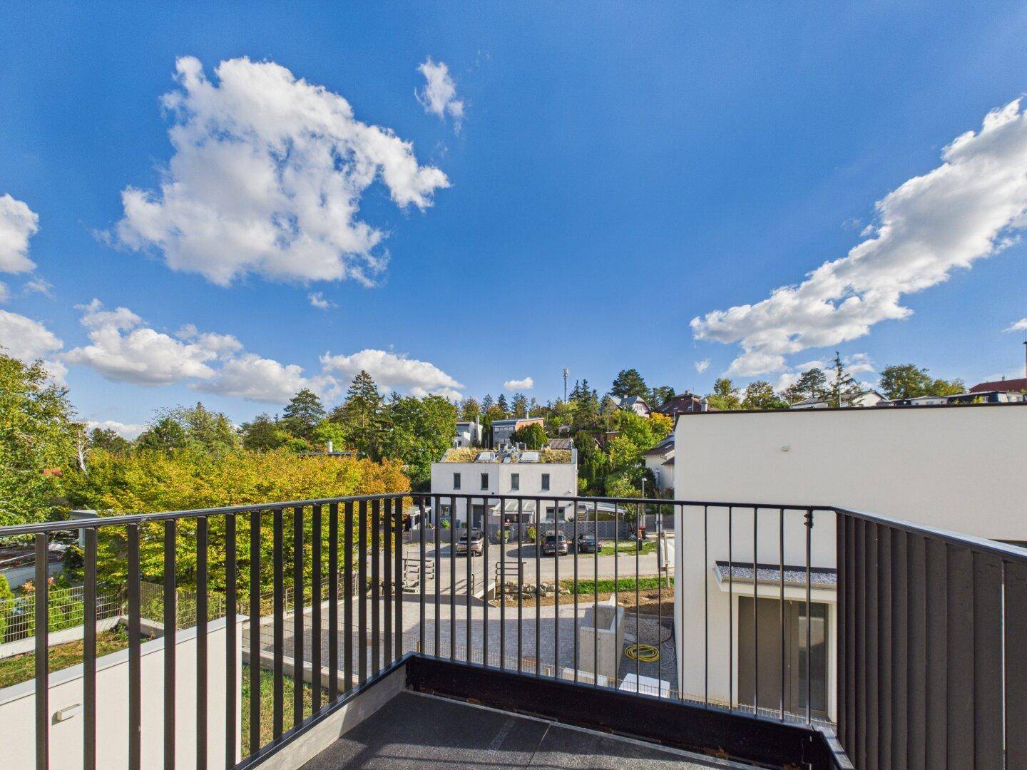 Balkon mit schwarzem Geländer und weitem Blick über die grüne Umgebung und Dächer.