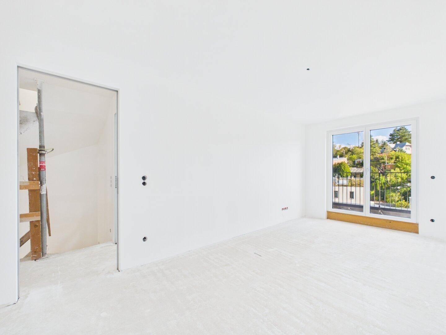 Geräumiges Schlafzimmer im Rohbau mit großen Fenstern und Blick auf die grüne Umgebung.
