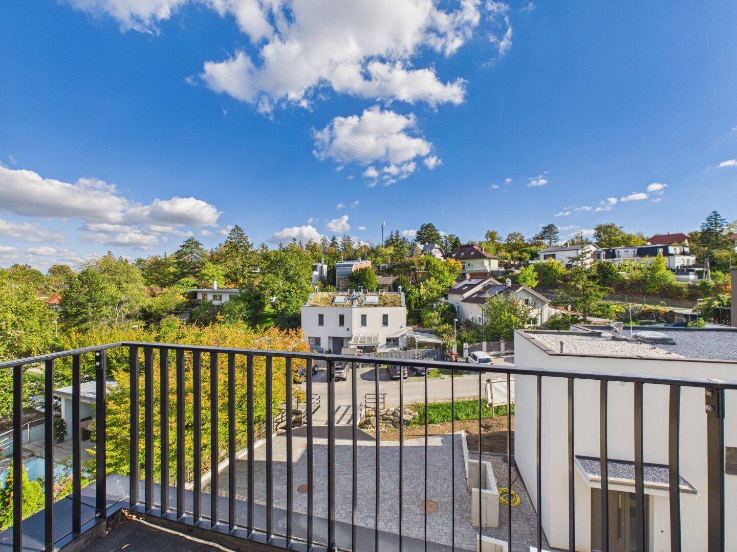 Balkon mit weitem Blick über die grüne Landschaft und die umliegenden Häuser unter blauem Himmel.