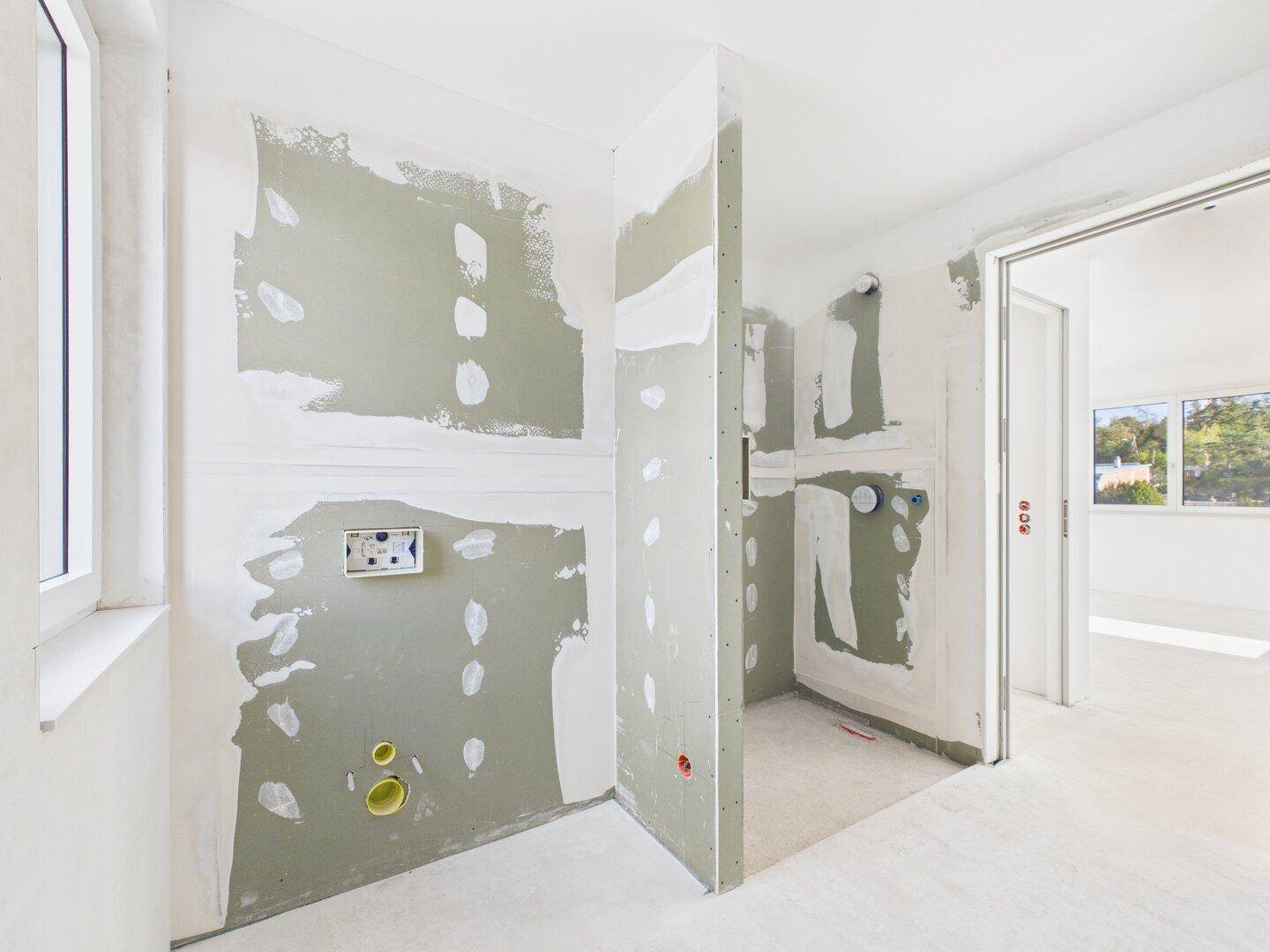 Badezimmer im Rohbau mit vorbereiteten Installationen für Dusche und Waschbecken.