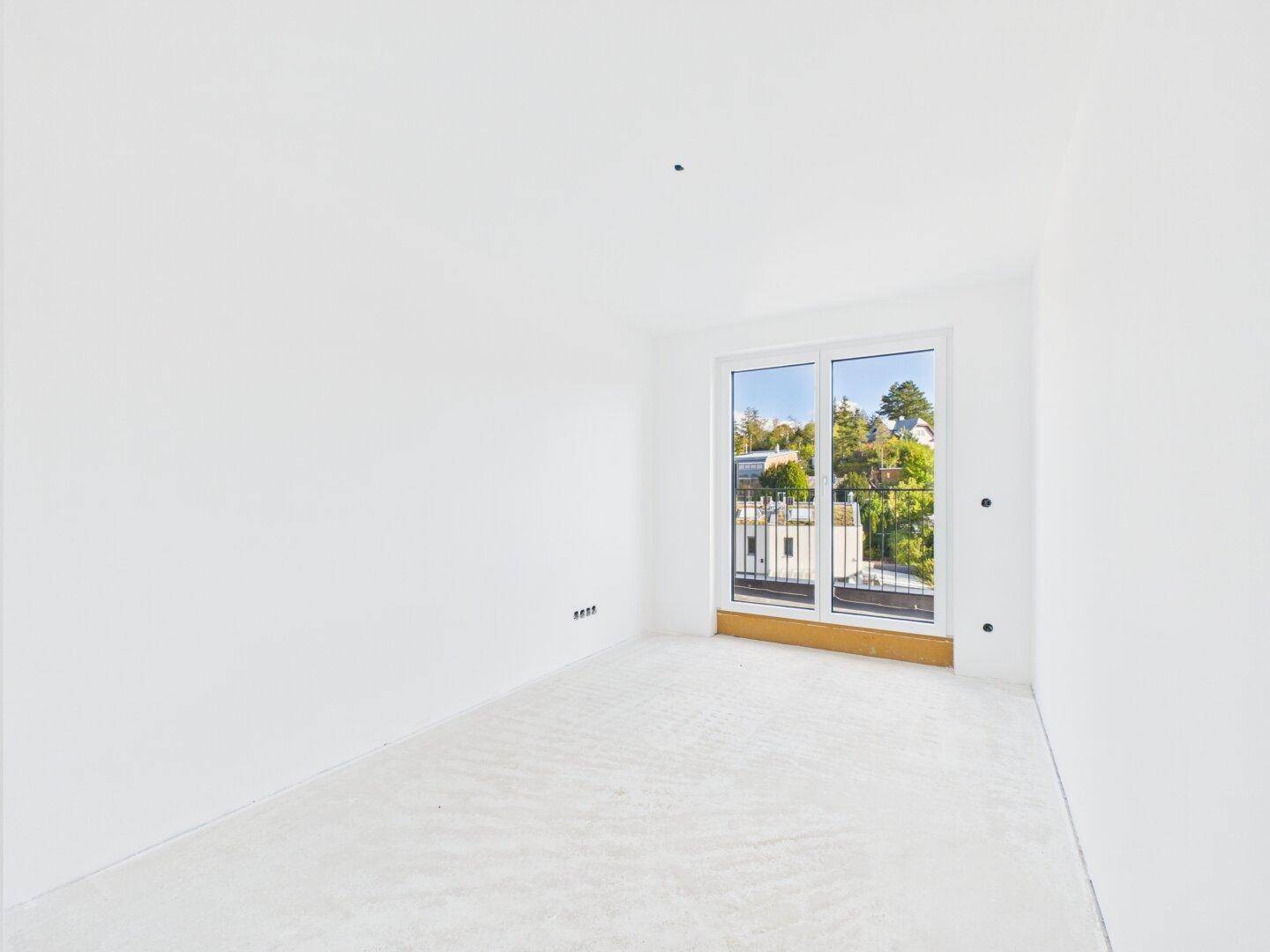 Helles Schlafzimmer im Rohbau mit Fensterfront und Zugang zu einem Balkon.