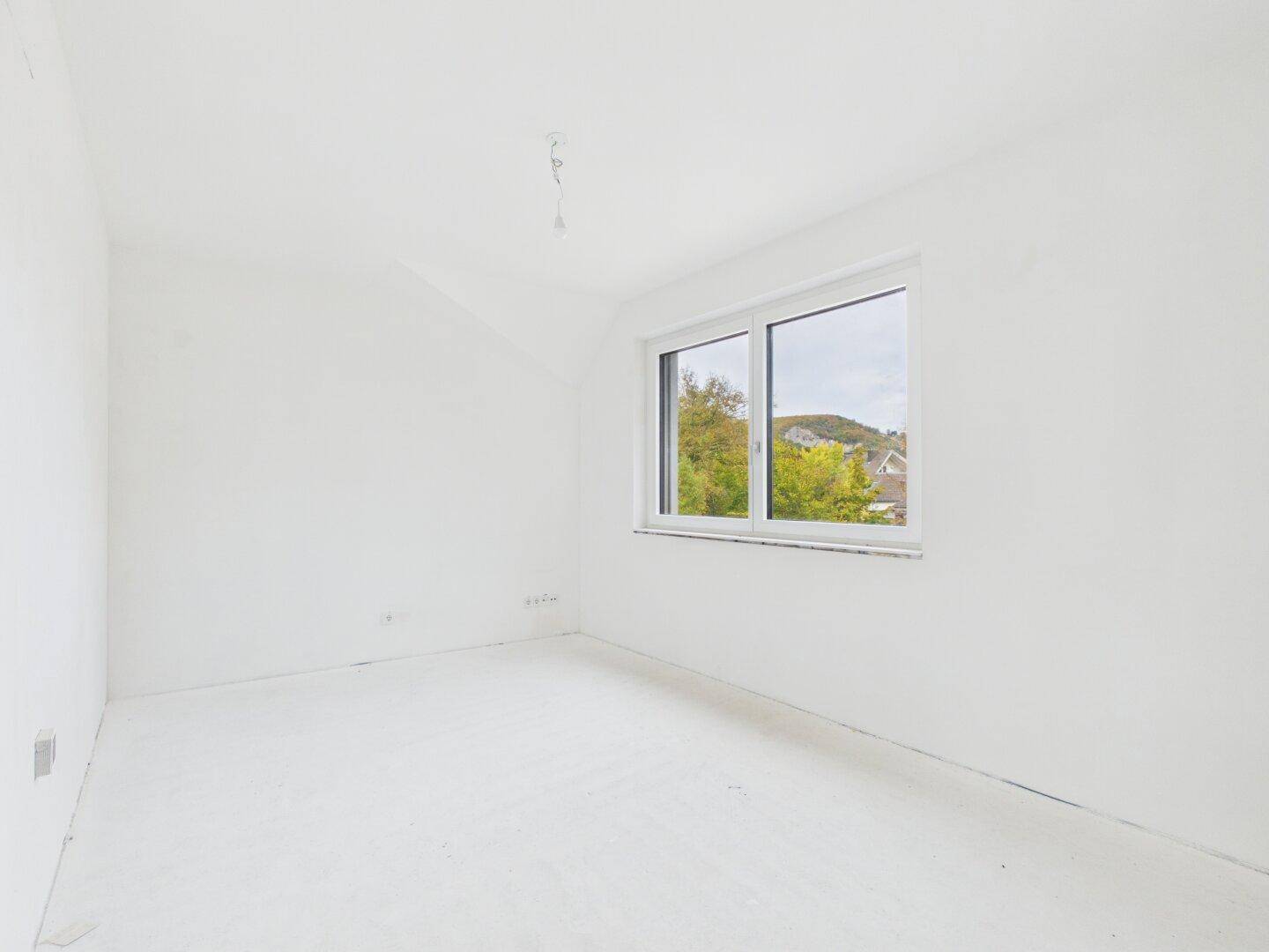 Unmöblierter Raum im Rohbau mit einem Fenster, das einen Blick auf die Umgebung bietet.