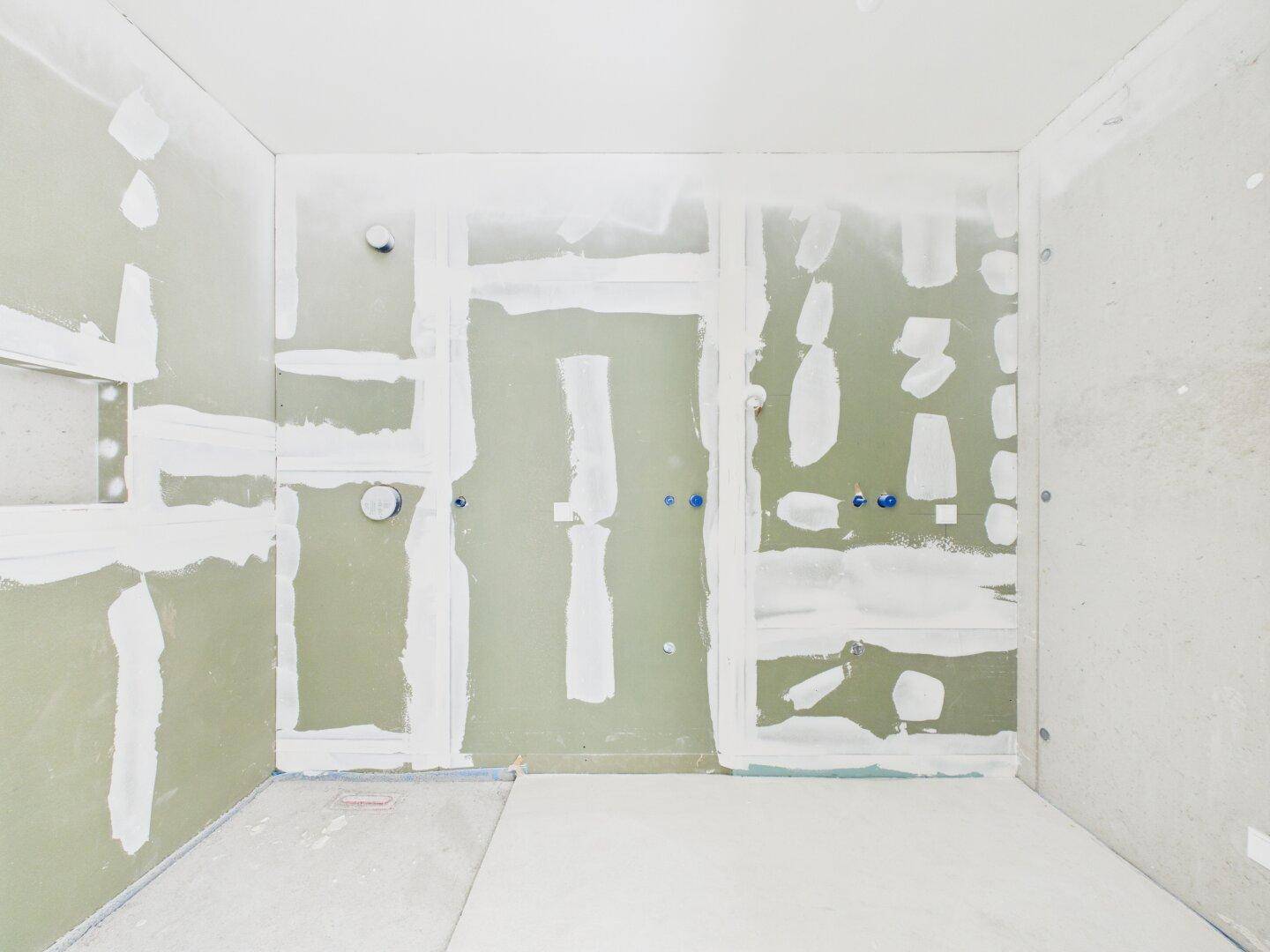 Badezimmer im Rohbau mit vorbereiteten Installationen und Trockenbauwänden, bereit für Fliesen.