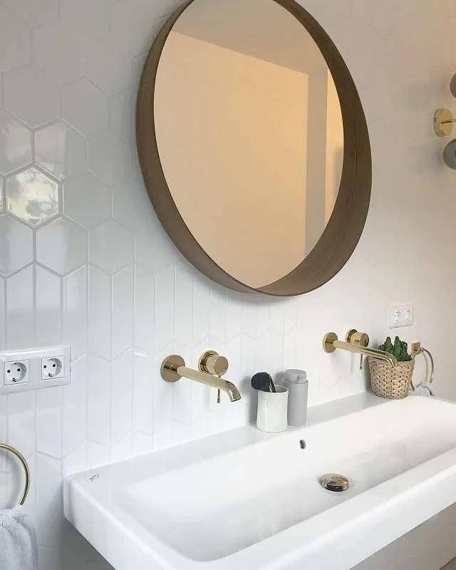 Modernes Badezimmer mit weißen Fliesen, goldenen Armaturen und rundem Spiegel über dem Waschbecken.