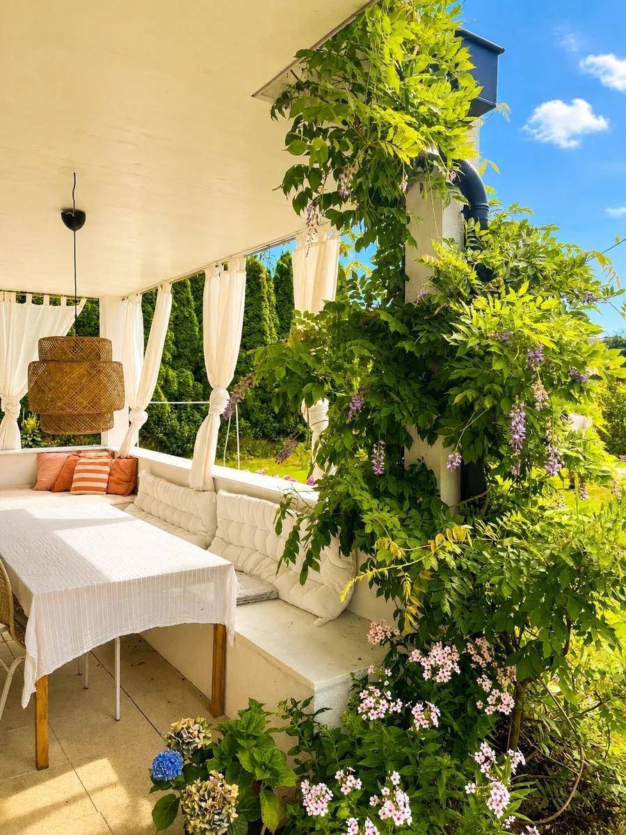 Grüne überdachte Terrasse mit Kletterpflanzen, Essbereich und Lounge-Möbeln.