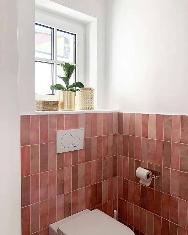 Gäste-WC mit rosafarbenen Fliesen, wandhängender Toilette und einem Fenster für Tageslicht.