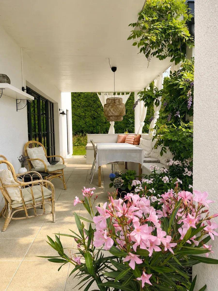 Gemütliche überdachte Terrasse mit Rattanmöbeln und blühenden Pflanzen.