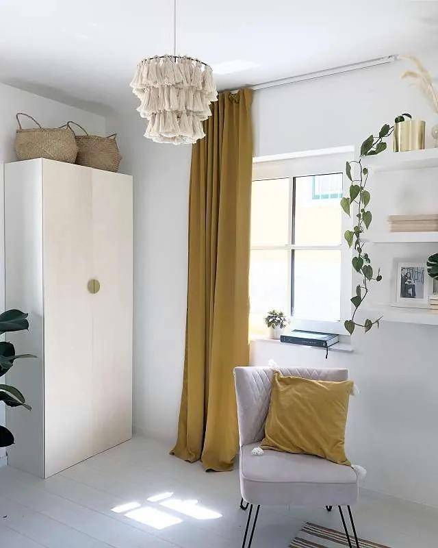 Helles Zimmer mit Schrank, Sessel und gelben Vorhängen.
