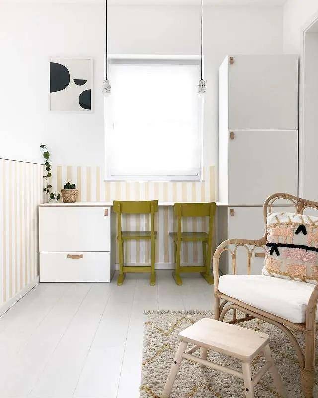 Heller Kinderzimmer oder Arbeitsbereich mit gelb-weiß gestreiften Wänden und kleinen Stühlen unter dem Fenster.