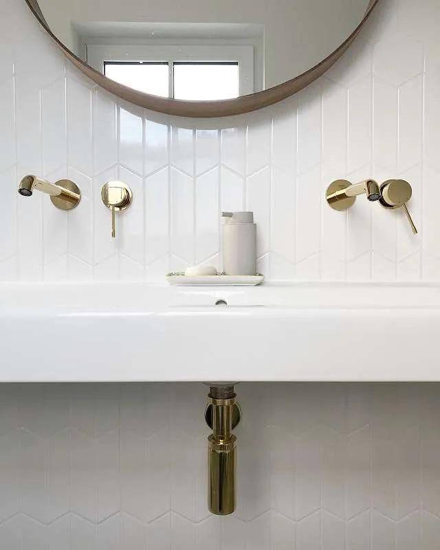 Modernes Badezimmer mit weißem Waschbecken, goldenen Armaturen und rundem Spiegel.