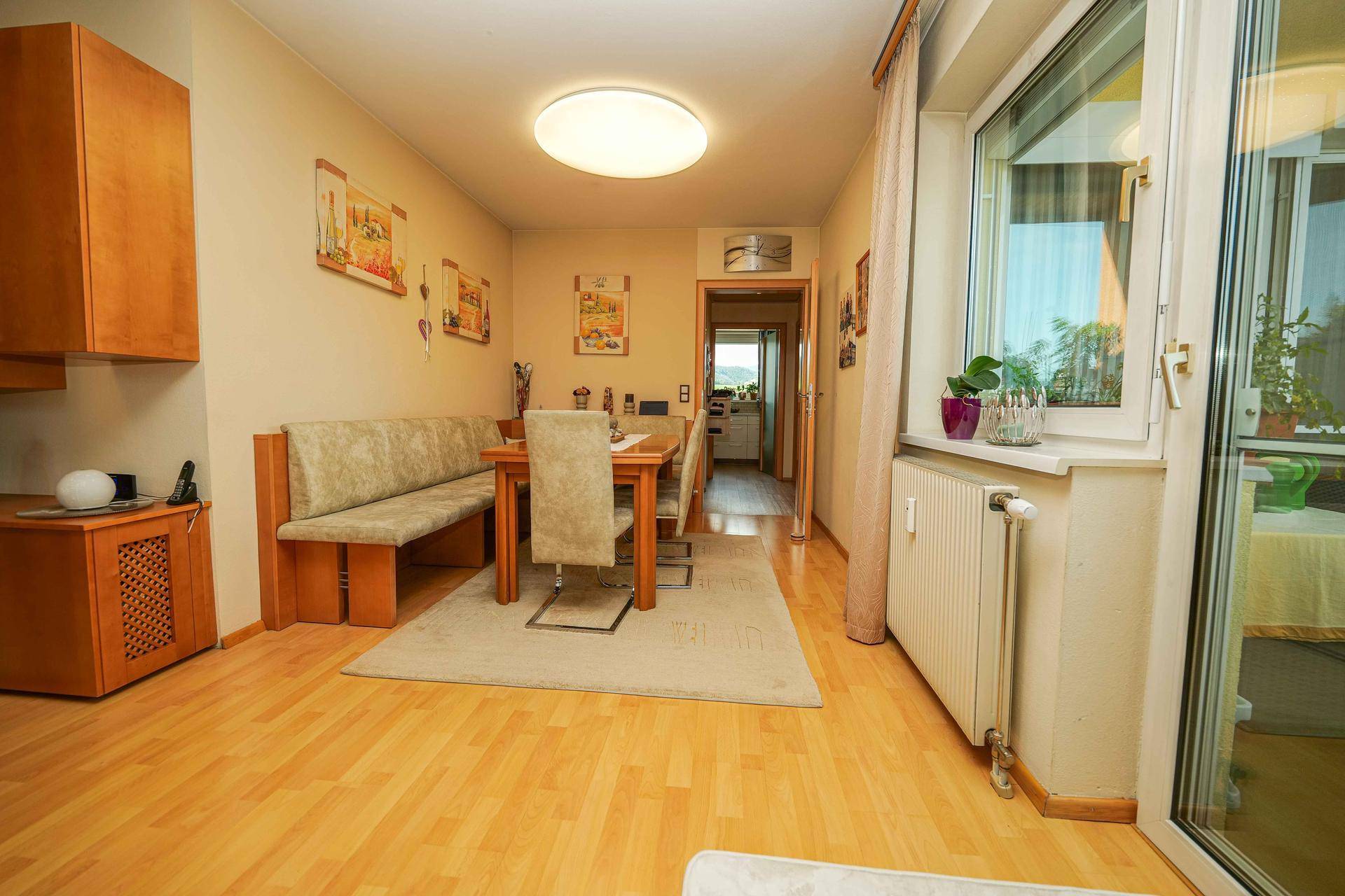 Heller Essbereich mit Holztisch, Sitzbank und Zugang zu einem verglasten Balkon.