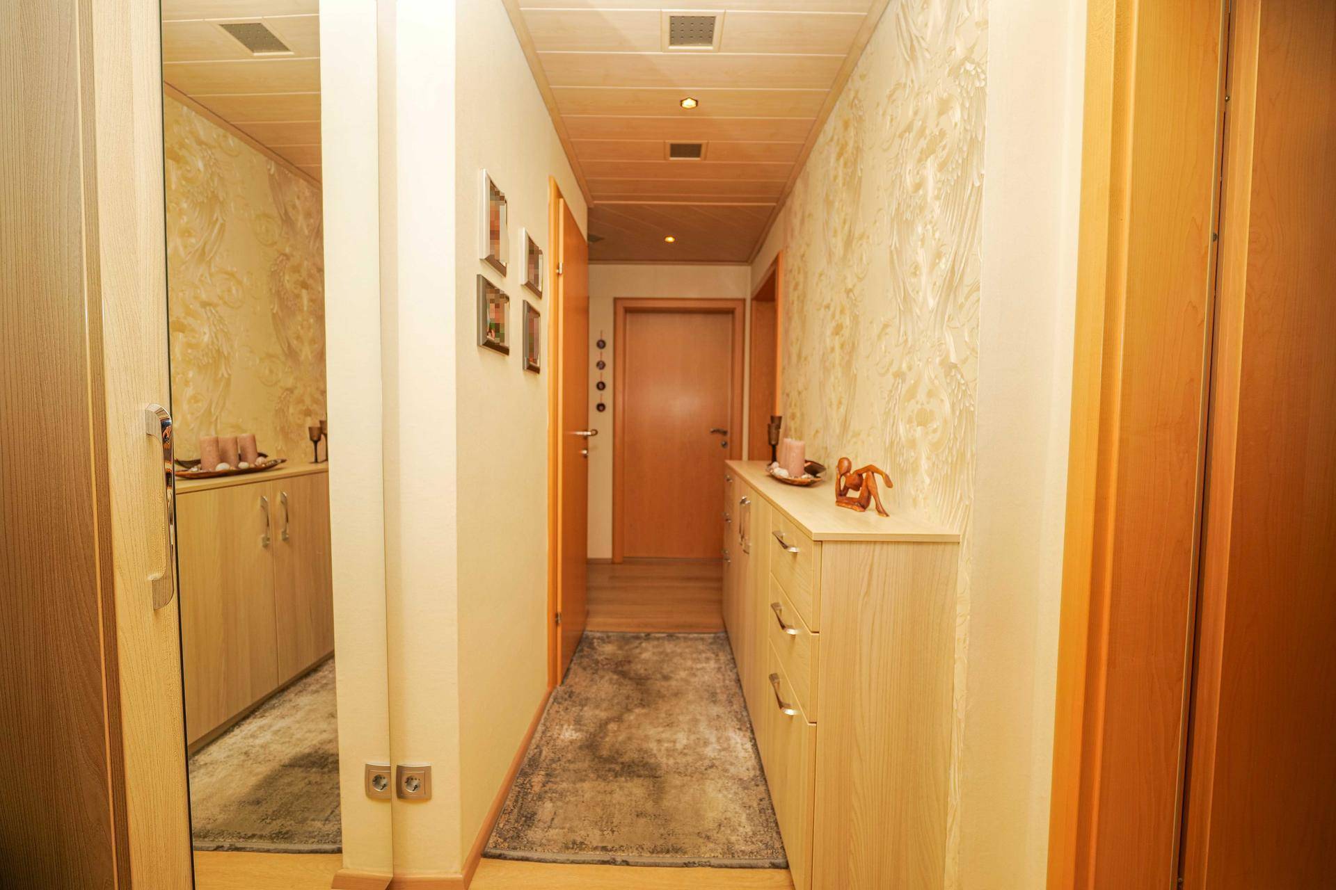 Langer Flur mit Holzboden, Deckenbeleuchtung und dezenter Tapete.