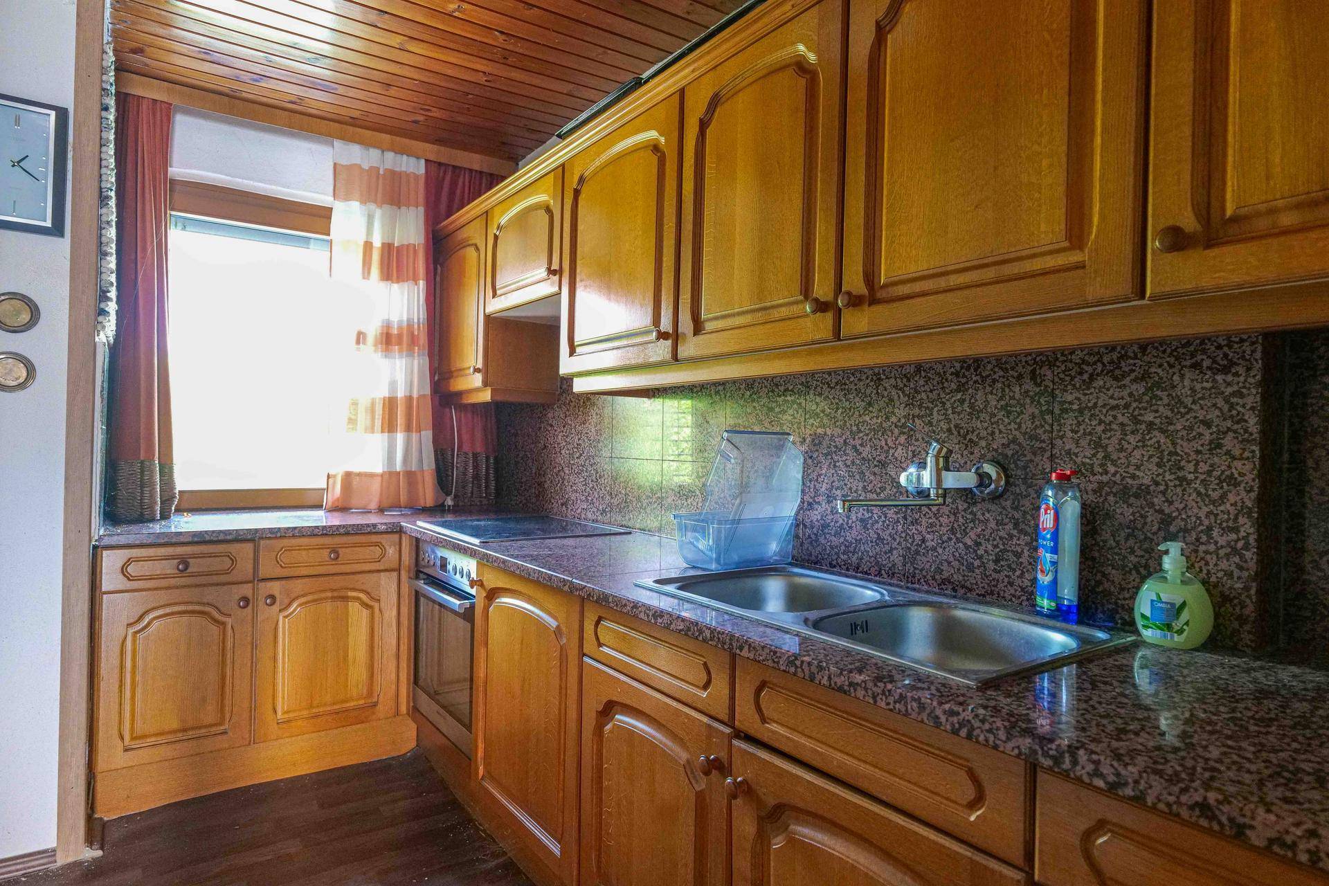 Traditionelle Holzküche mit Granitarbeitsplatten, Doppelspüle und Fenster mit Vorhängen.