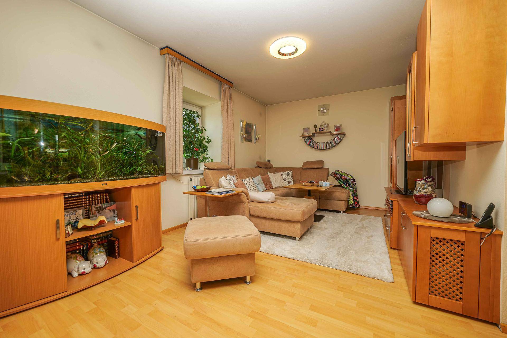 Gemütliches Wohnzimmer mit beigem Sofa, großem Aquarium und hellem Holzboden.