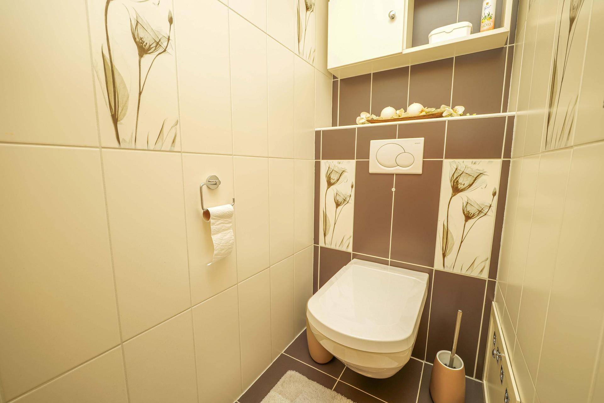 Separates WC mit Wand-WC und dekorativen Fliesen in warmen Farbtönen.