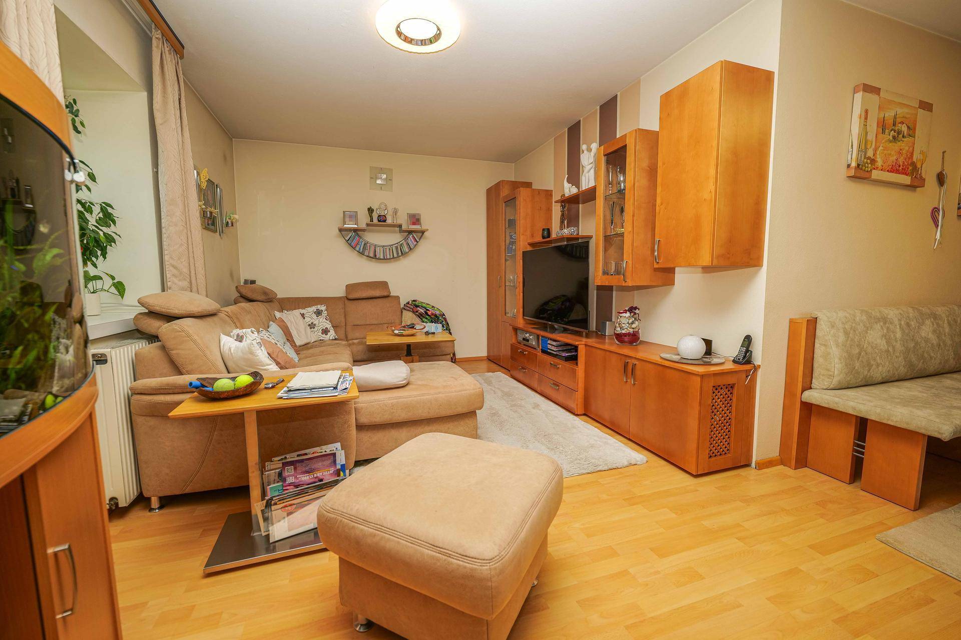 Wohnzimmer mit beigem Sofa, TV-Möbeln und hellem Holzboden.