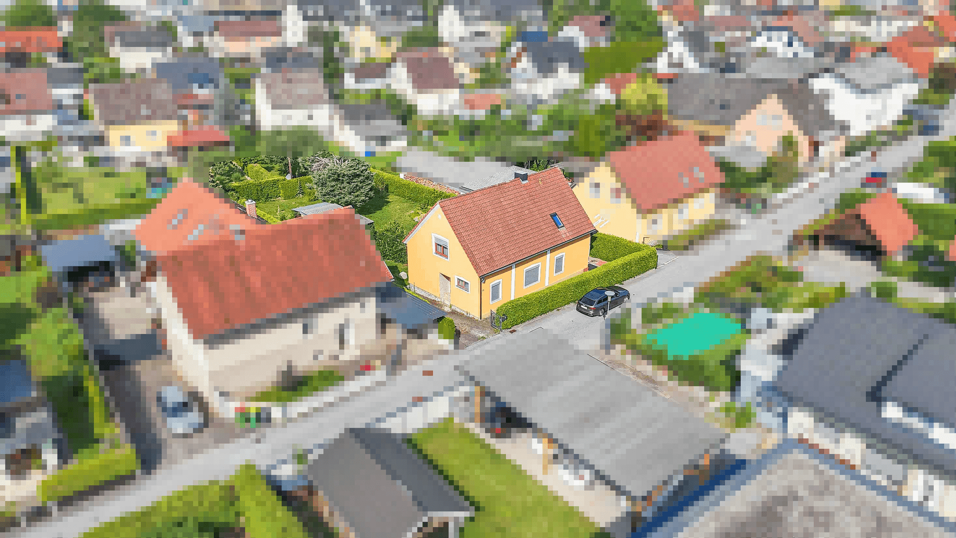Luftaufnahme des gelben Einfamilienhauses in einer Wohnsiedlung mit umliegenden Gärten und Straßen.
