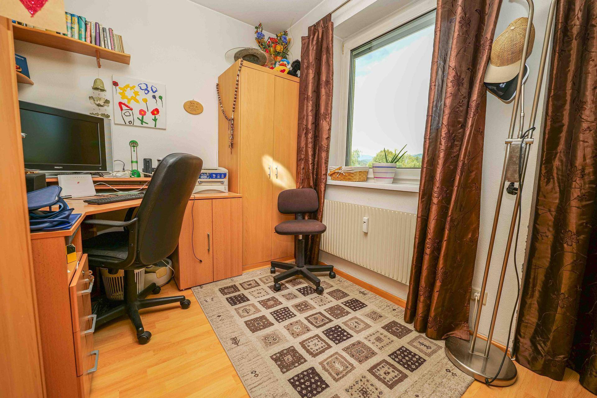 Funktionales Arbeitszimmer mit Schreibtisch, Bürostuhl und Fenster mit Blick ins Grüne.